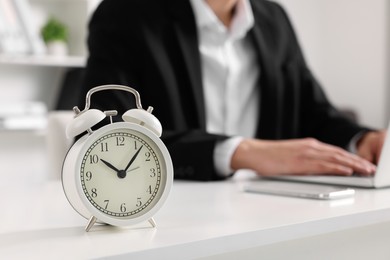 Photo of White alarm clock and man working at table in office, closeup with space for text. Deadline concept