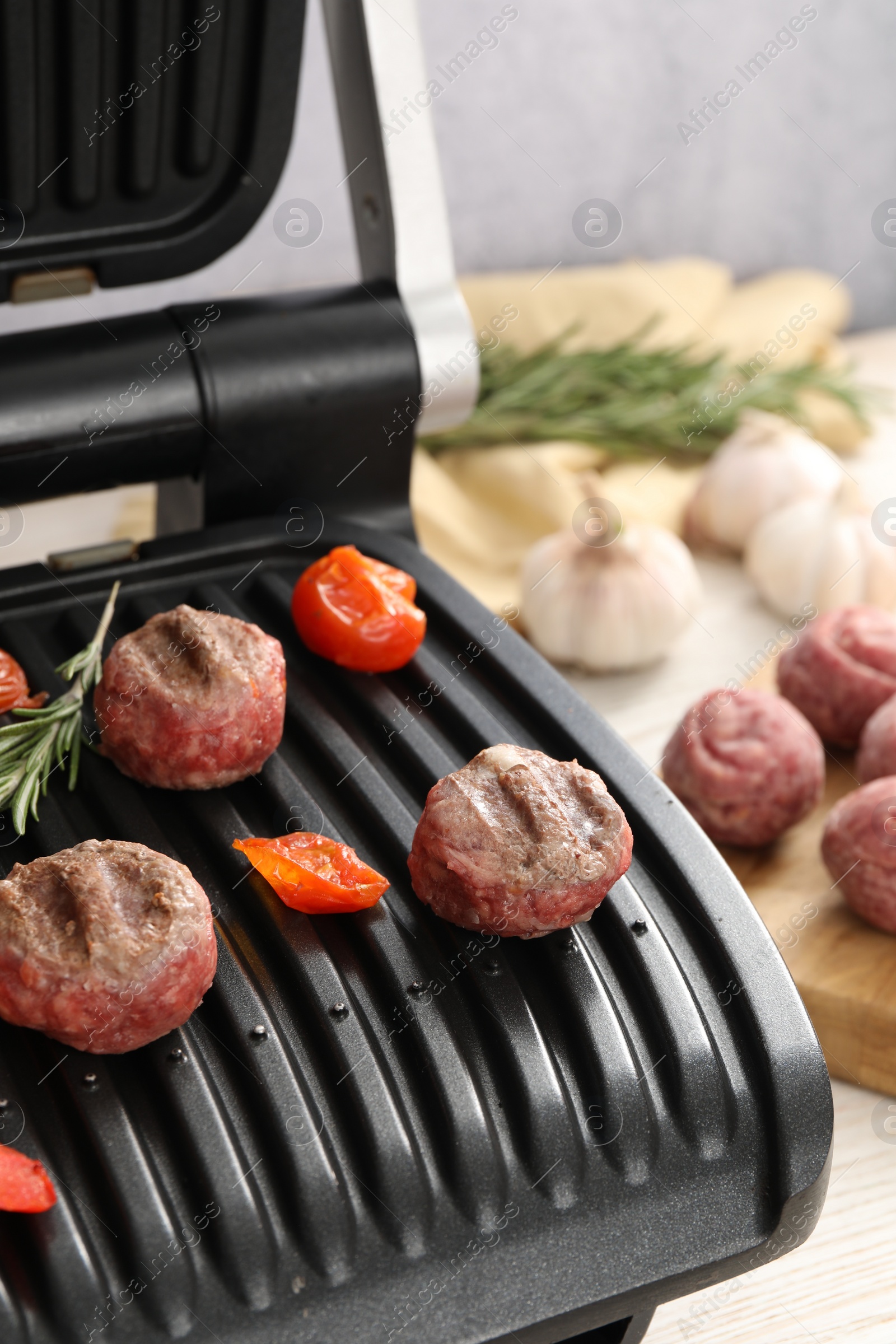 Photo of Electric grill with vegetables and meat balls on table, closeup