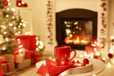 Photo of Red cup and festive lights on white table in room with Christmas decorations. Interior design