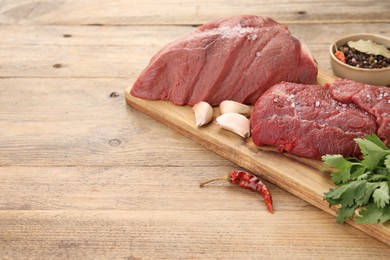 Pieces of raw beef meat, chili pepper, garlic and spices on wooden table, space for text