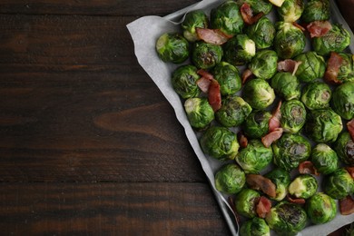 Photo of Delicious roasted Brussels sprouts and bacon in baking dish on wooden table, top view. Space for text