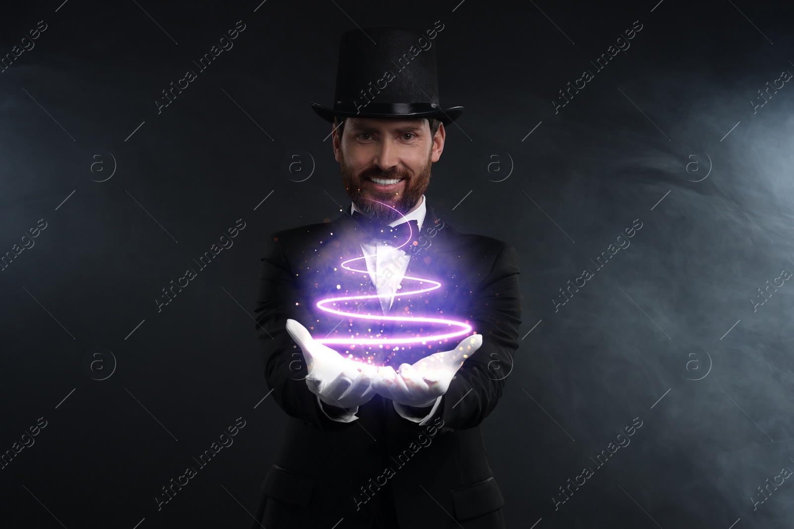 Image of Magic and sorcery. Magician with fantastic light in smoke on dark background