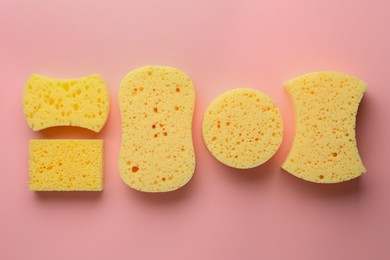 New yellow sponges of different shapes on pink background, flat lay