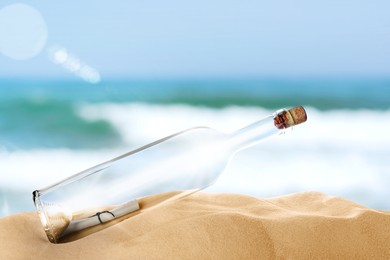 Image of Corked glass bottle with rolled paper note on sandy beach near ocean