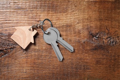 Keys with keychain in shape of house on wooden table, top view. Space for text