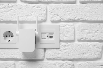 Wireless Wi-Fi repeater on white brick wall, space for text
