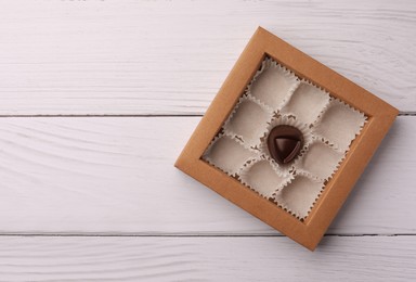 Photo of Partially empty box of chocolate candies on white wooden table, top view. Space for text