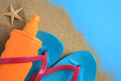 Photo of Flip flops, sunscreen and sand on light blue background, flat lay with space for text. Beach accessories