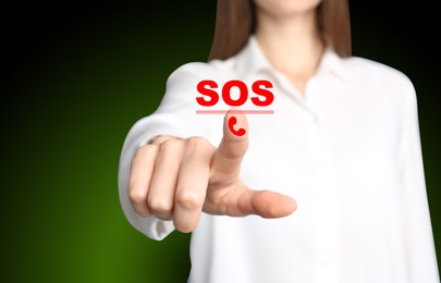 Image of Young woman pressing virtual SOS button in case of danger on green background, closeup