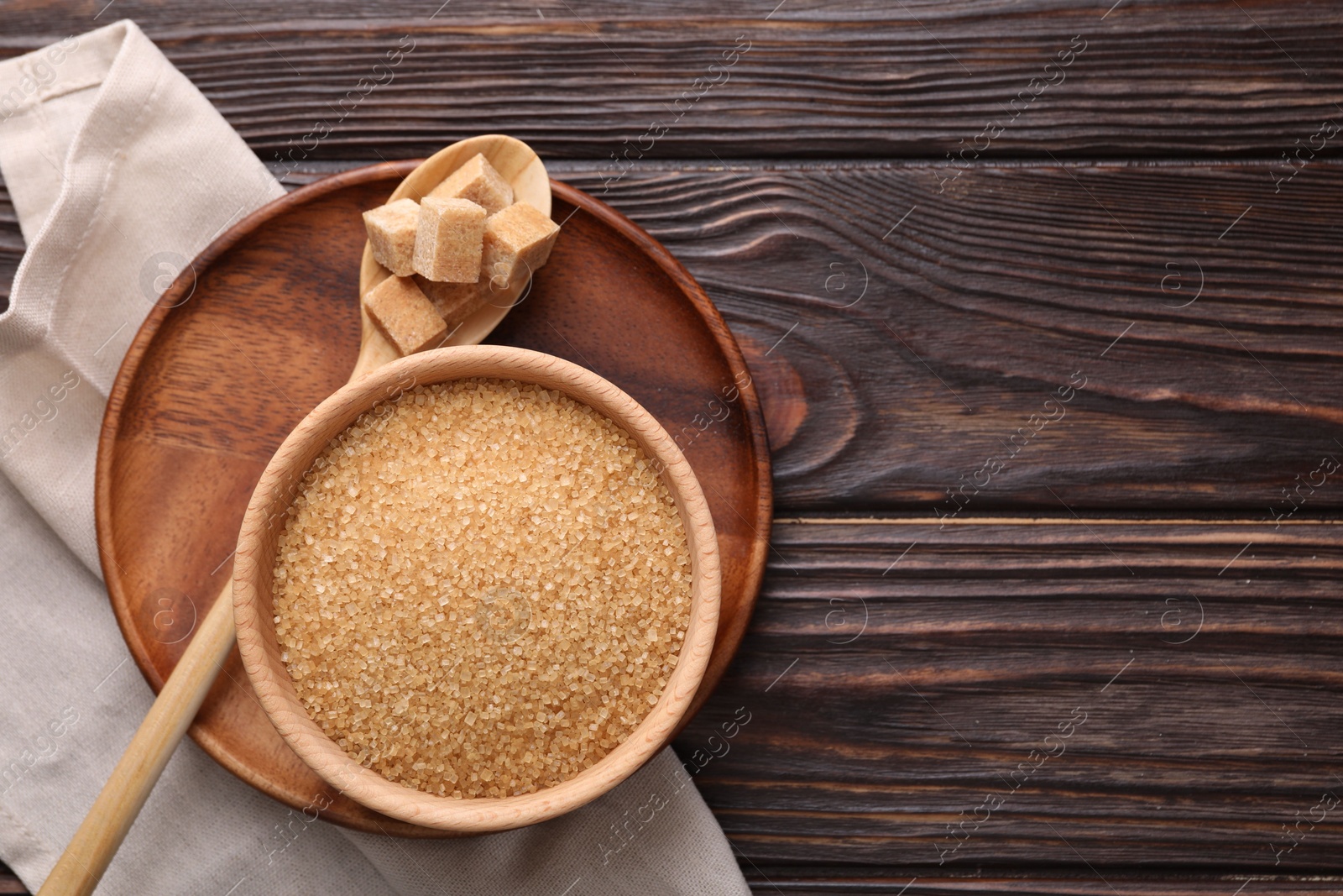 Photo of Bowl and spoon with brown sugar on wooden table, top view. Space for text