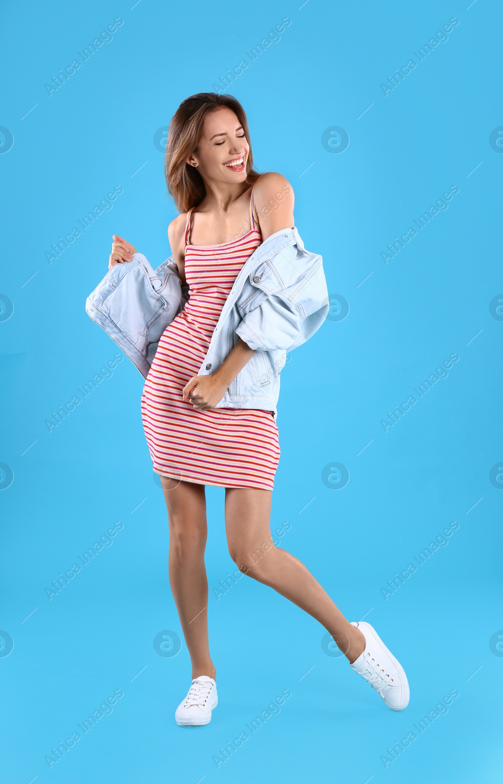 Photo of Beautiful young woman in dress and jacket dancing on blue background