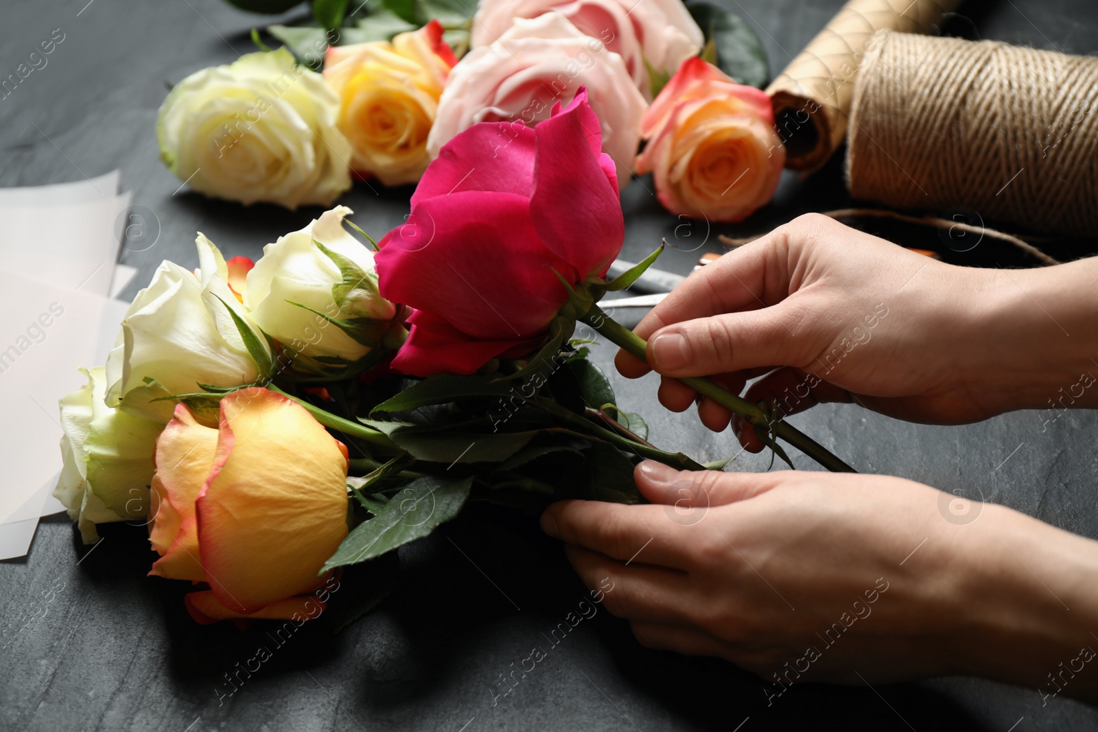 Photo of Woman making luxury bouquet of fresh roses at black table, closeup