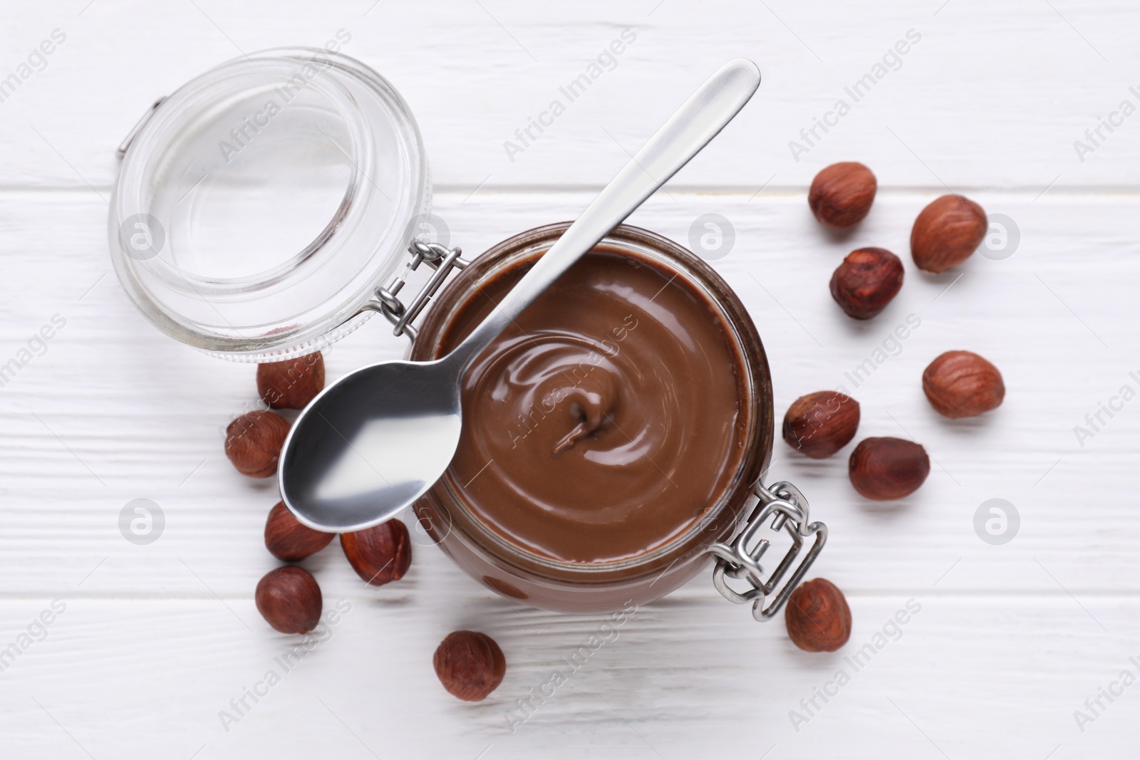 Photo of Jar with delicious chocolate paste and nuts on white wooden table, flat lay