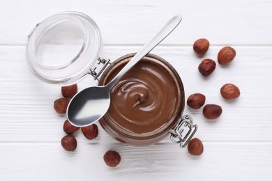 Photo of Jar with delicious chocolate paste and nuts on white wooden table, flat lay