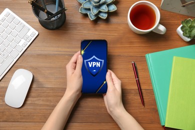 Image of Woman using smartphone with switched on VPN at wooden table, top view