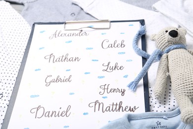 Photo of Clipboard with different baby names and toy on child's clothes, closeup