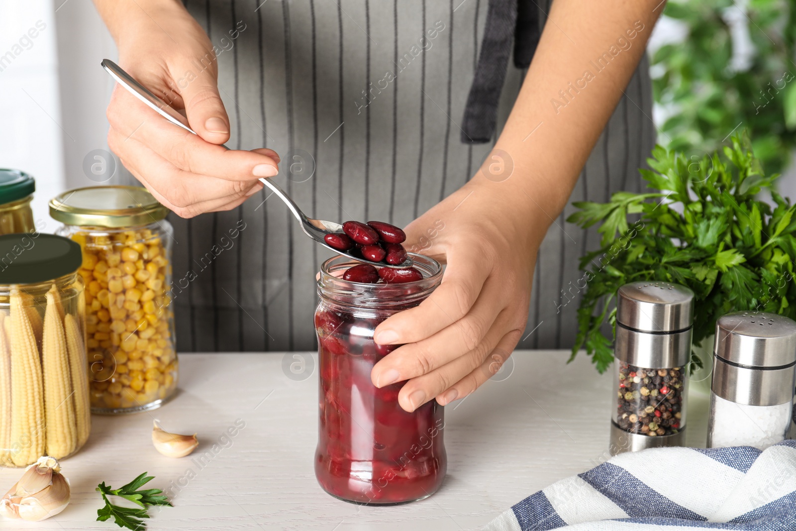 Photo of Woman putting beans into jar at white table, closeup