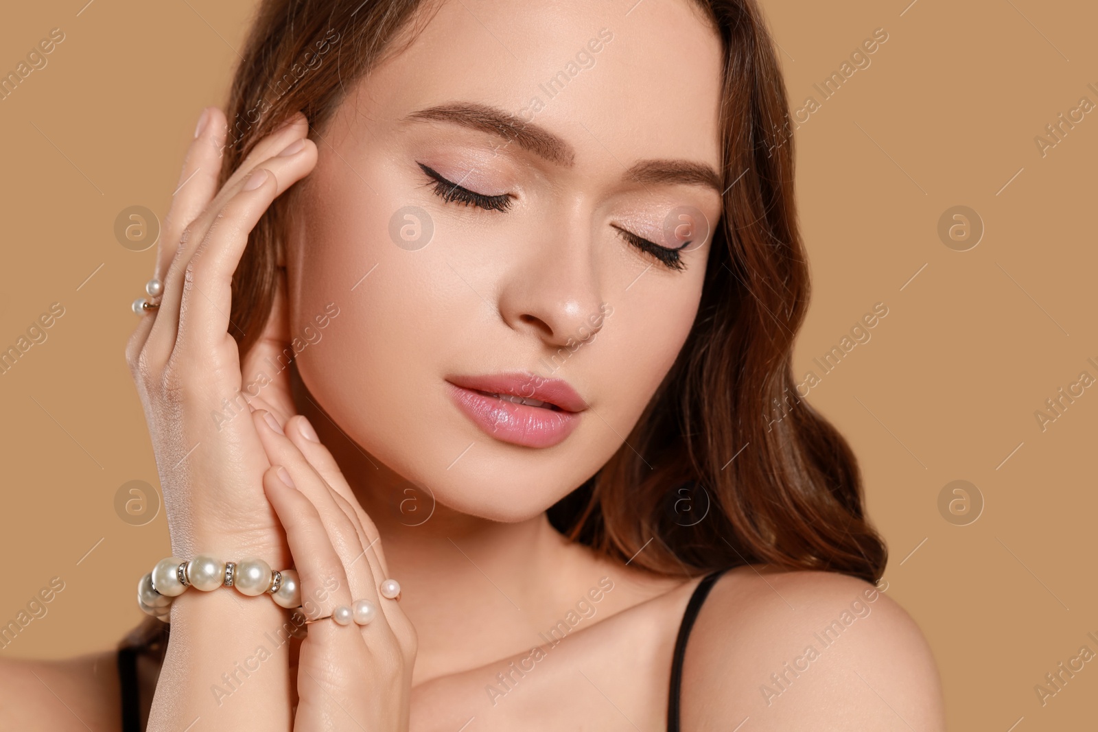 Photo of Young woman wearing elegant pearl jewelry on brown background, closeup