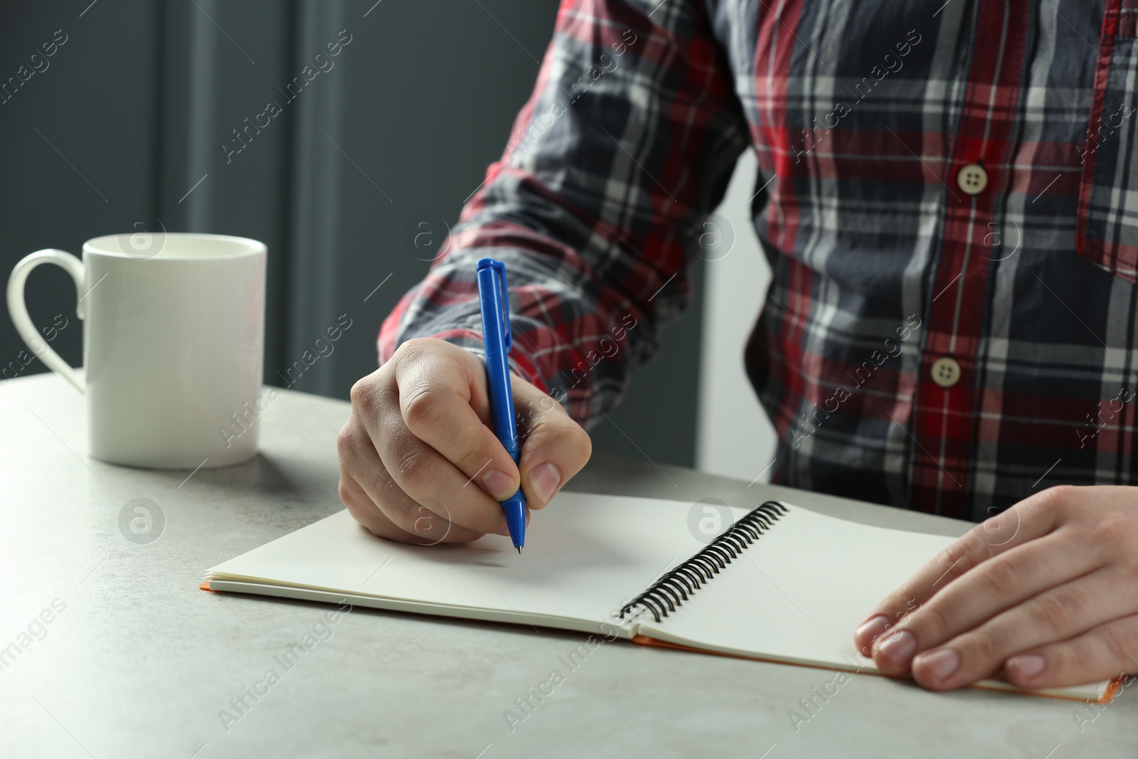 Photo of Man writing with pen in notebook at white table, closeup