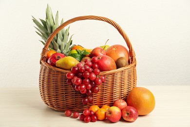 Wicker basket with different fresh fruits on white wooden table