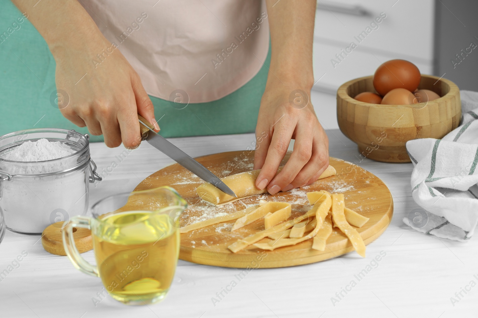 Photo of Making homemade pasta. Woman cutting dough at white wooden table, closeup