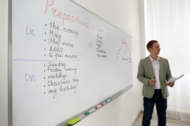 Photo of English teacher giving lesson on prepositions of time near whiteboard in classroom