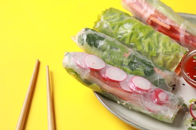 Delicious spring rolls and chopsticks on yellow background, closeup