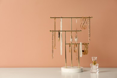 Photo of Holder with set of luxurious jewelry and perfume on white table near pale pink wall, space for text