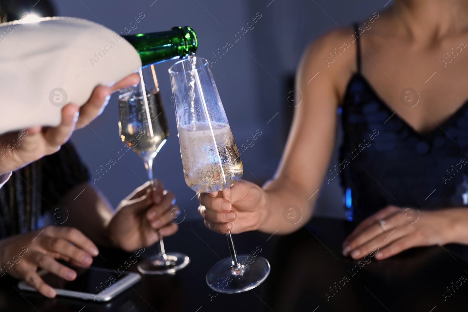 Photo of Waiter pouring champagne from bottle into woman's glass at bar, closeup