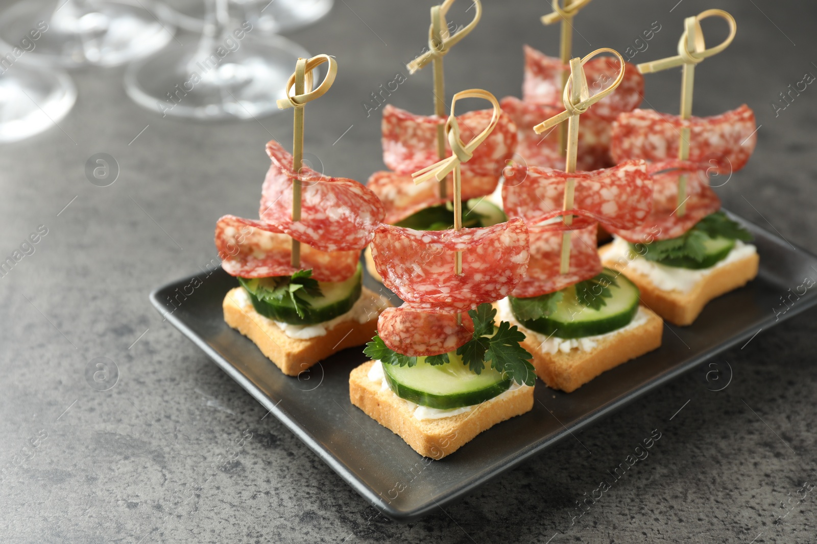 Photo of Tasty canapes with salami, cucumber and cream cheese on grey table