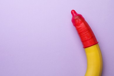 Photo of Banana with condom on lilac background, top view and space for text. Safe sex concept