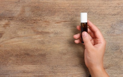 Woman with bottle of essential oil on wooden background, closeup. Space for text