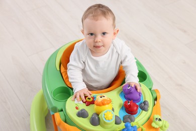 Portrait of cute little boy in baby walker on wooden floor