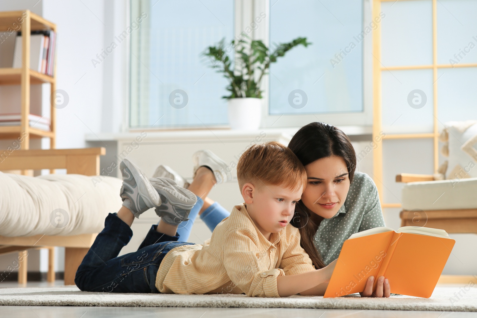 Photo of Mother reading book with her son on floor in living room at home