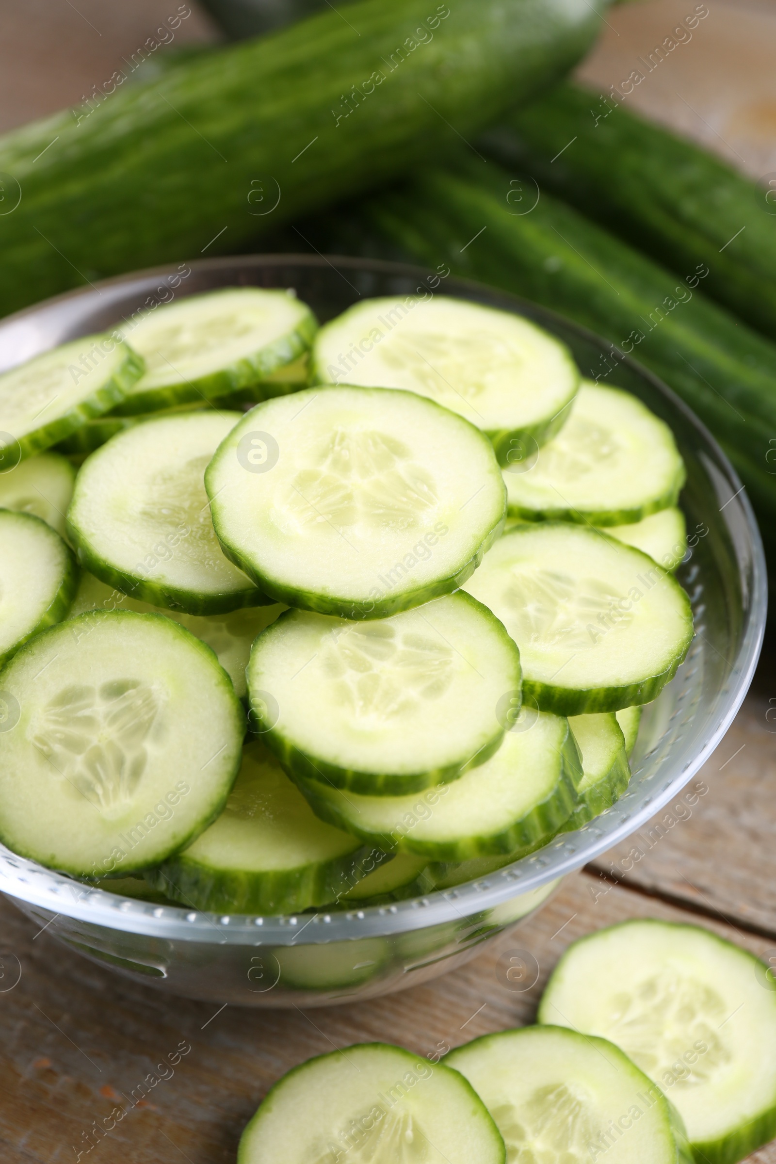 Photo of Cut cucumber in glass bowl and fresh vegetables on wooden table, closeup