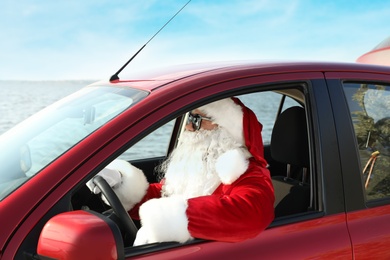 Photo of Authentic Santa Claus with sunglasses driving car, view from outside