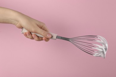 Woman holding whisk with whipped cream on pink background, closeup