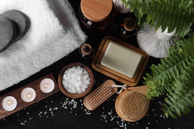 Flat lay composition with different spa products and burning candles on black table