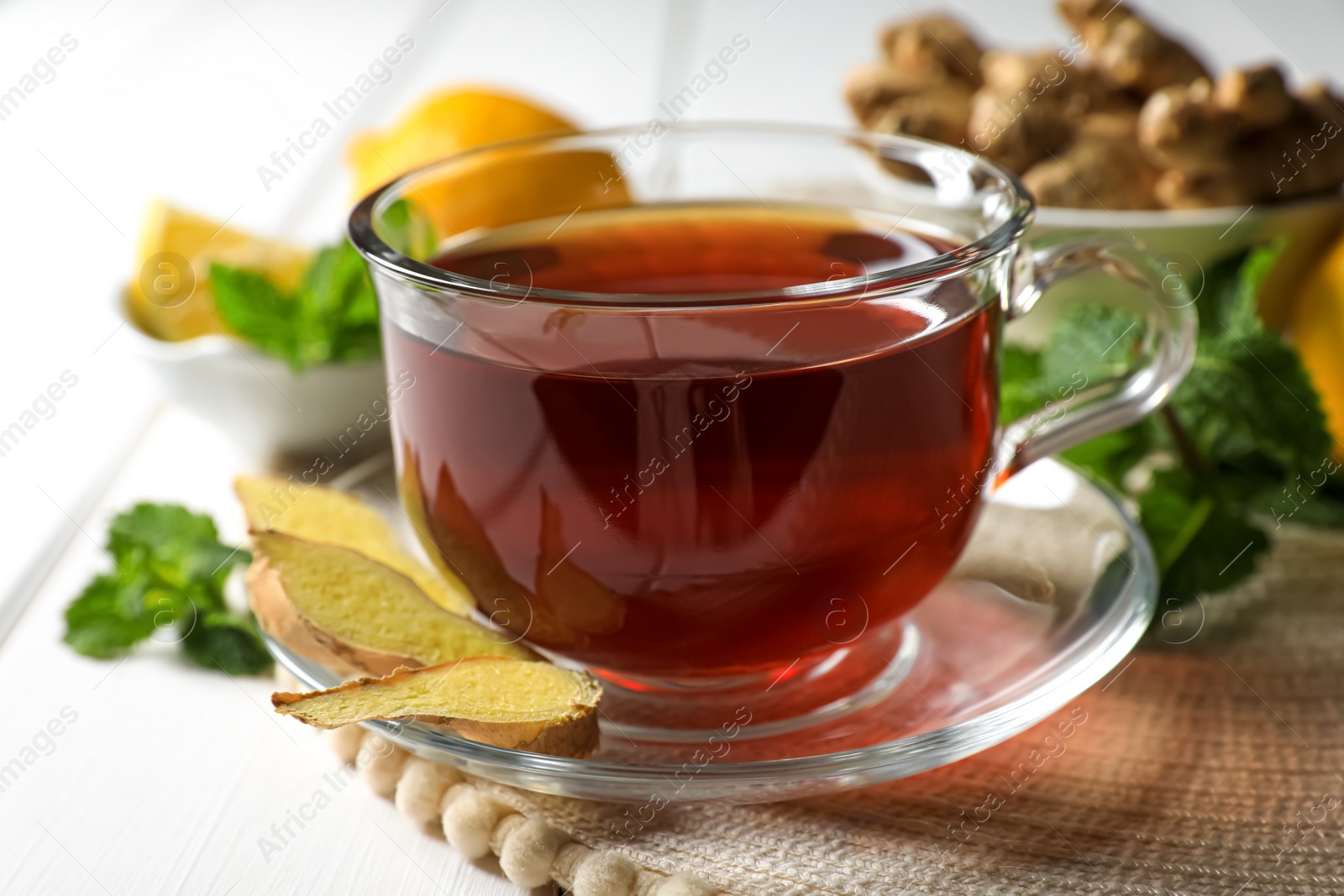 Photo of Cup of delicious ginger tea and ingredients on white wooden table, closeup