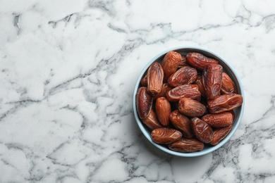 Bowl with sweet dried date fruits on marble background, top view. Space for text