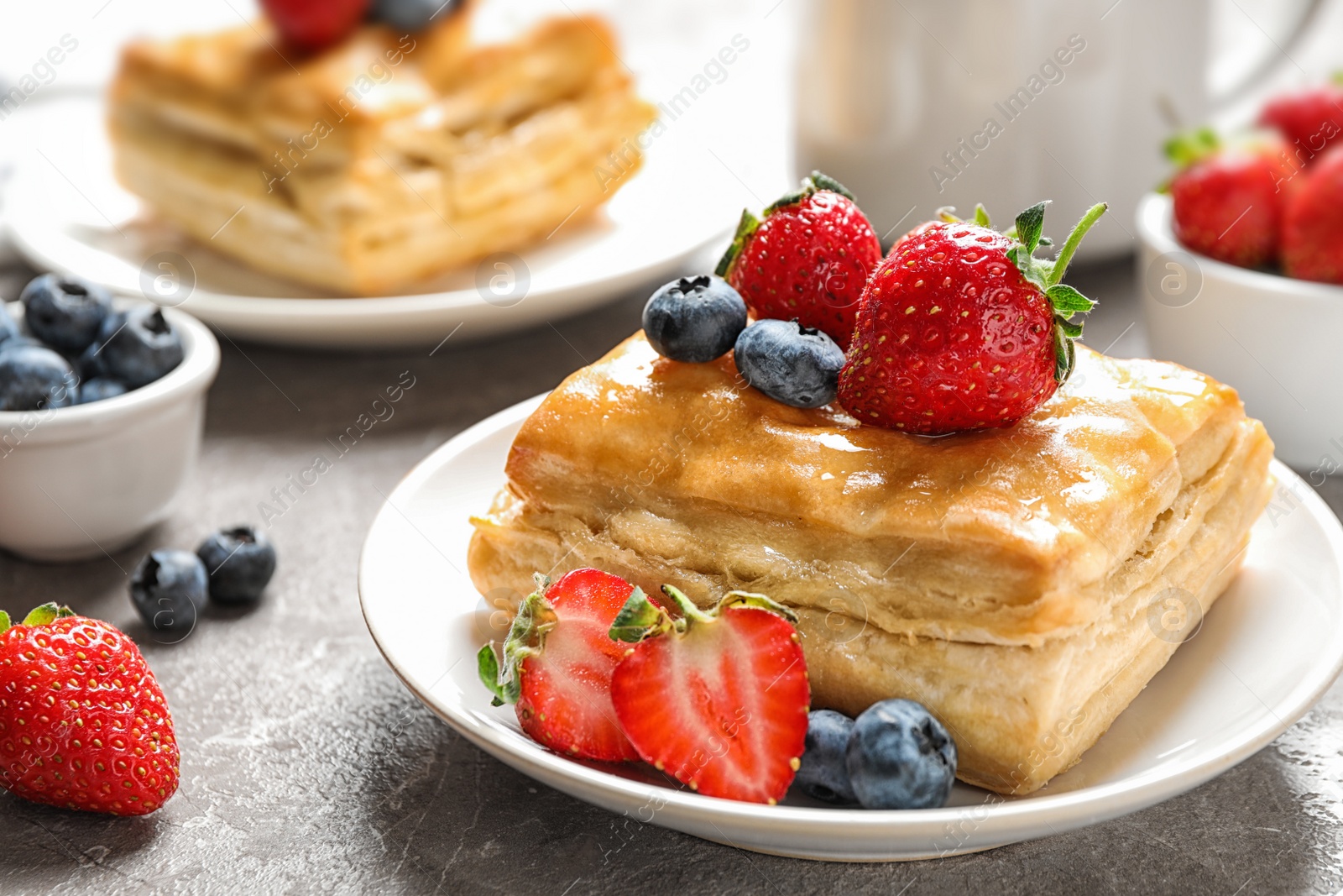 Photo of Fresh delicious puff pastry with sweet berries on grey marble table, closeup