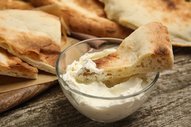 Photo of Piece of fresh pita bread with cream cheese on wooden table, closeup