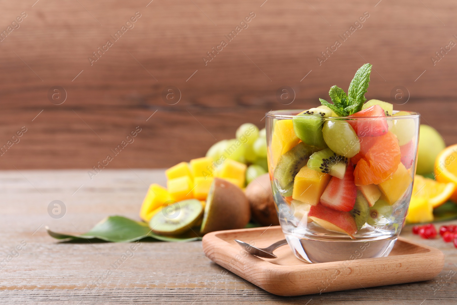 Photo of Delicious fresh fruit salad in dish on wooden table, space for text