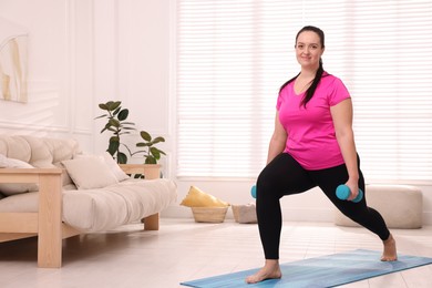 Photo of Overweight woman doing exercise with dumbbells at home, space for text