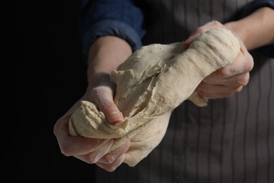 Photo of Making bread. Woman kneading dough on dark background, closeup. Space for text