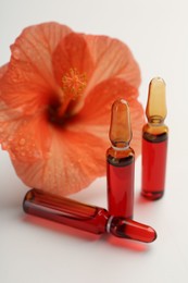 Photo of Skincare ampoules and hibiscus flower on white background, closeup