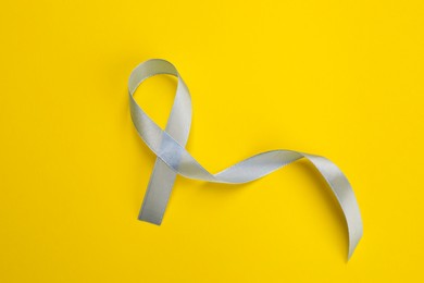 Photo of International Psoriasis Day. Ribbon as symbol of support on yellow background, top view