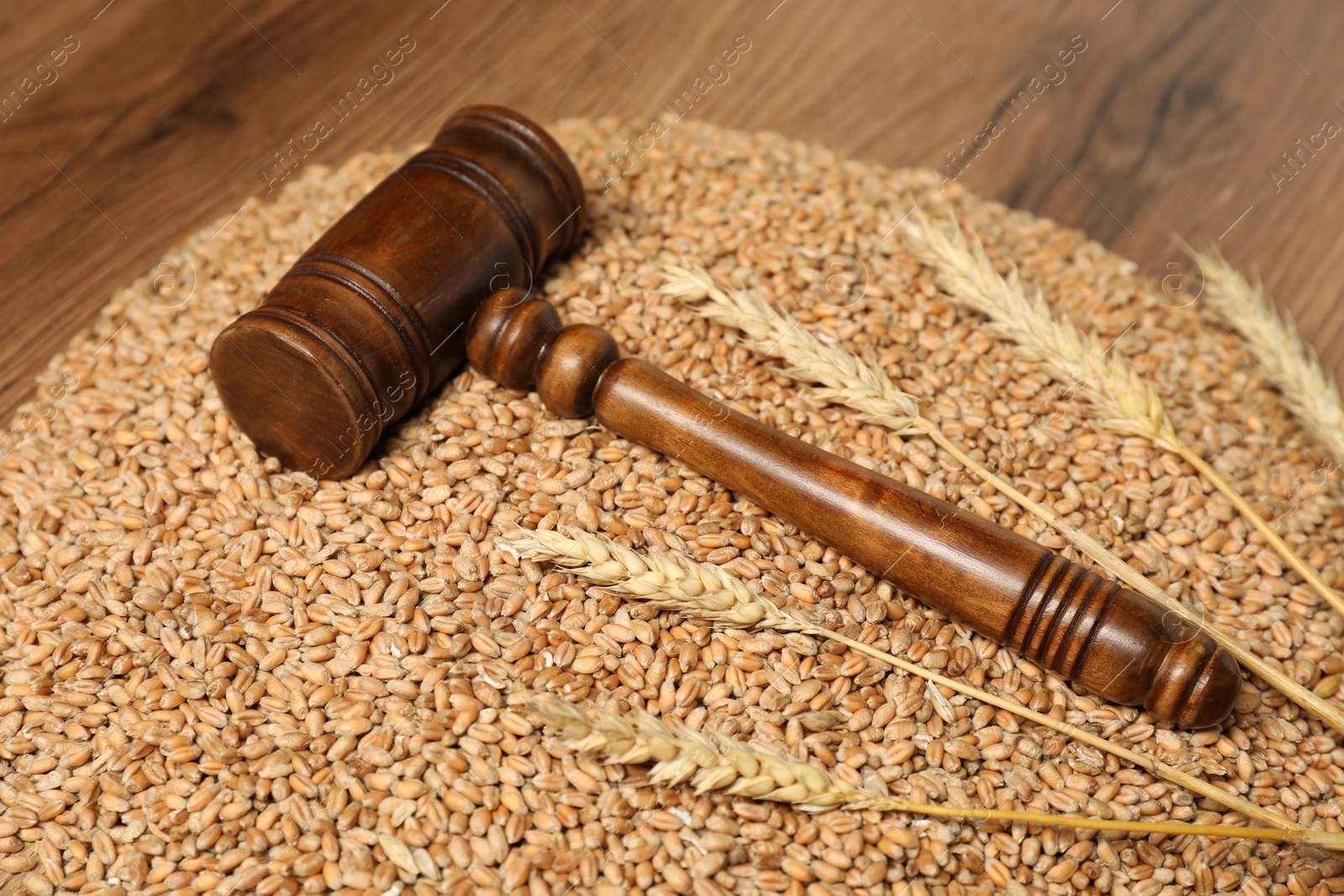 Photo of Judge's gavel, wheat ears and grains on wooden table. Agricultural deal