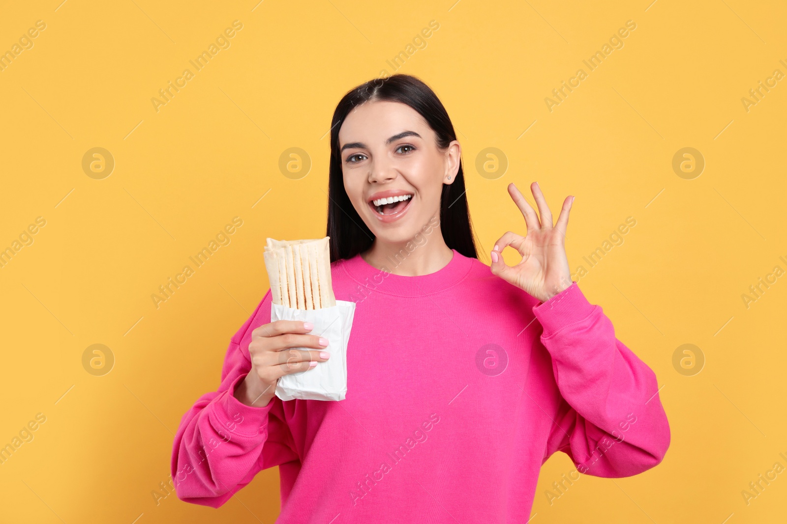 Photo of Happy young woman with delicious shawarma on yellow background