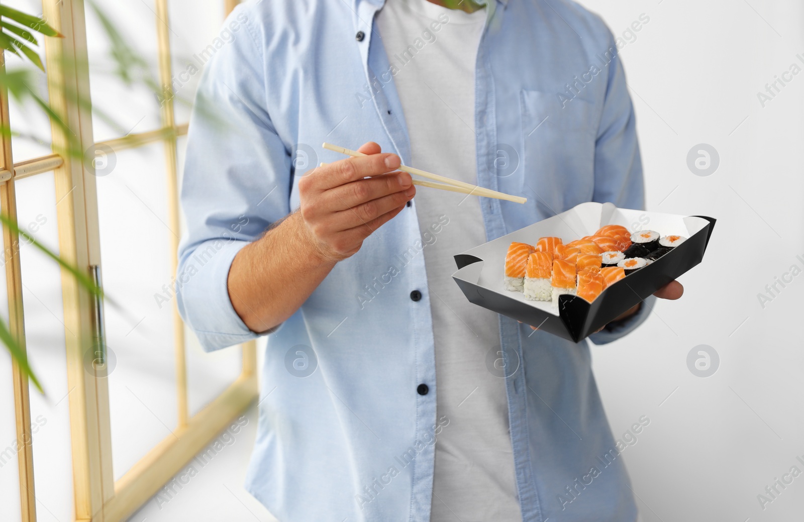 Photo of Man eating sushi rolls with chopsticks indoors, closeup